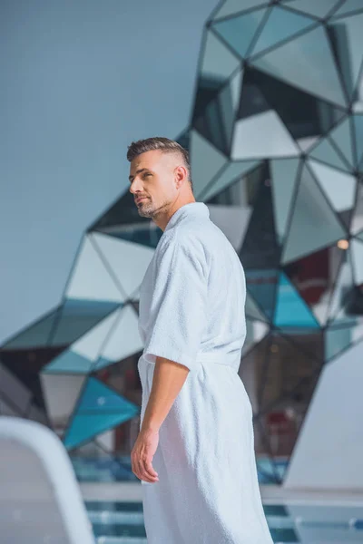 Handsome man standing in white bathrobe — Stock Photo