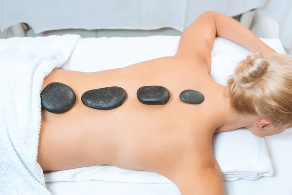 Costas de mulher loira com pedras quentes na mesa de massagem — Fotografia de Stock