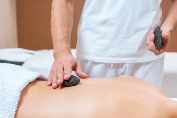 Primer plano de masajista masculino poniendo piedras calientes en la espalda de la mujer - foto de stock