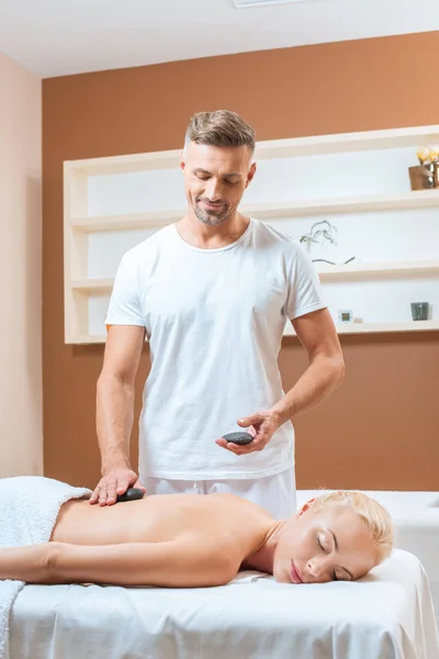 Handsome therapist doing stone massage in spa salon — Stock Photo