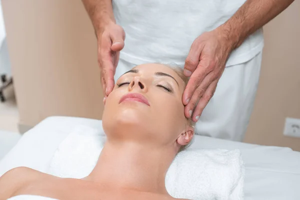 Masajista masculino haciendo masaje facial a mujer en salón de spa - foto de stock