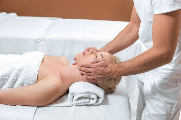 Maschio massaggiatore fare massaggio viso a donna in spa stanza — Foto stock