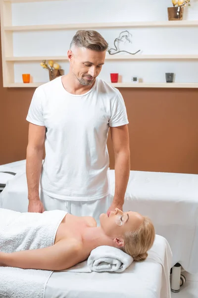 Masajista guapo mirando a la mujer rubia en el salón de spa - foto de stock