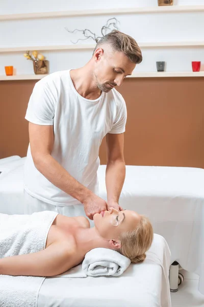 Schöner Masseur, der Augenklappen auf das Gesicht einer Frau aufträgt — Stockfoto