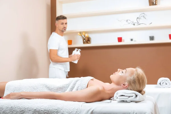 Masseur tenant bouteilles tandis que la femme couché sur la table de massage — Photo de stock
