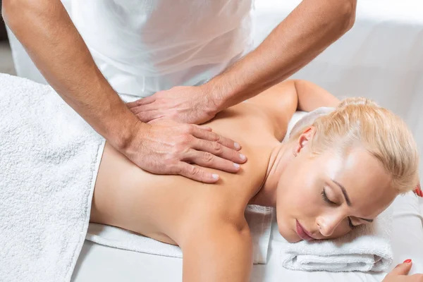 Masajista masculino haciendo masaje de espalda a mujer atractiva en spa - foto de stock