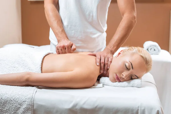 Masajista masculino haciendo masaje a hermosa mujer con los ojos cerrados en spa - foto de stock