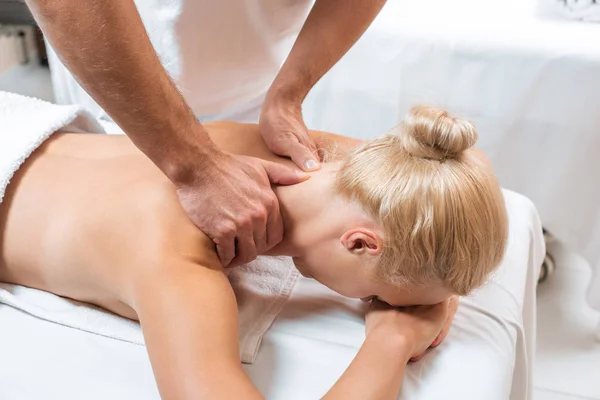 Masajista masculino haciendo masaje de cuello a mujer rubia en spa - foto de stock