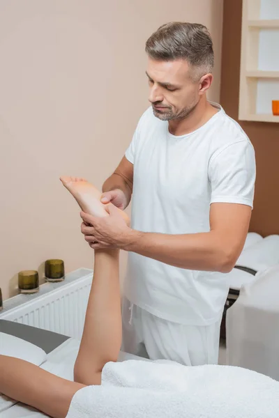 Handsome masseur massaging woman foot in spa — Stock Photo