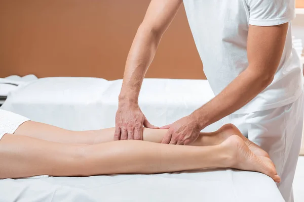 Vista ritagliata di uomo massaggiare gambe donna in spa — Foto stock