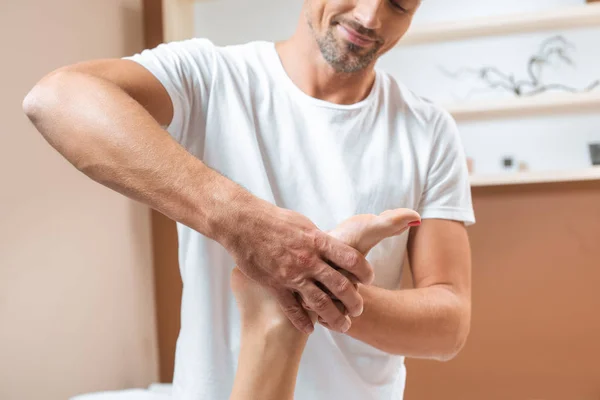 Handsome smiling masseur massaging woman foot in spa — Stock Photo