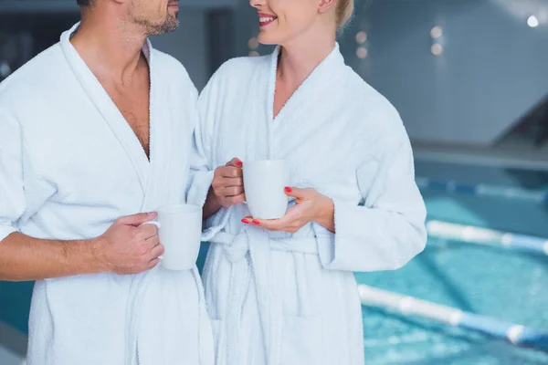 Vista ritagliata di uomo e donna allegro in piedi vicino alla piscina con tazze — Stock Photo