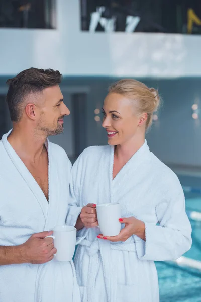 Lächelnder Mann und Frau mit Tassen am Swimmingpool — Stockfoto
