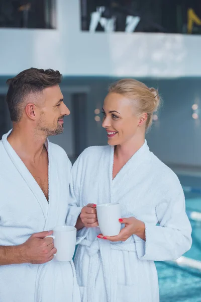 Smiling man and woman standing near swimming pool with cups — Stock Photo