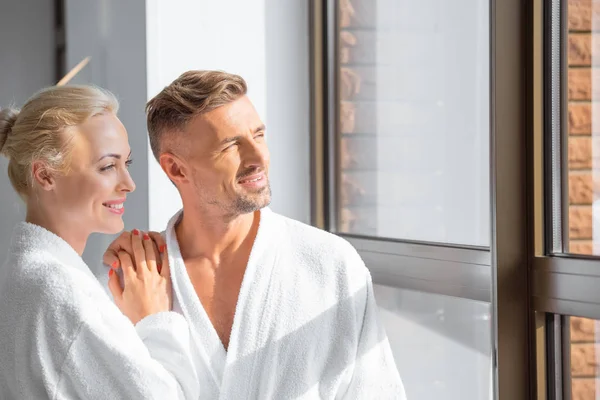Cheerful adult couple hugging and looking at window in spa — Stock Photo