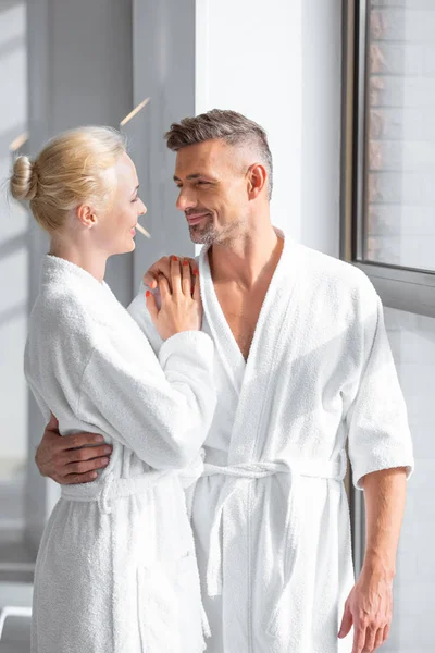 Smiling couple standing near window and hugging in spa — Stock Photo