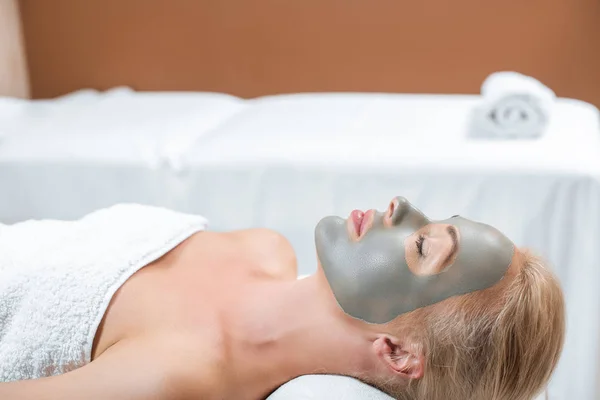 Bella donna bionda sdraiata con maschera di argilla facciale in spa — Foto stock