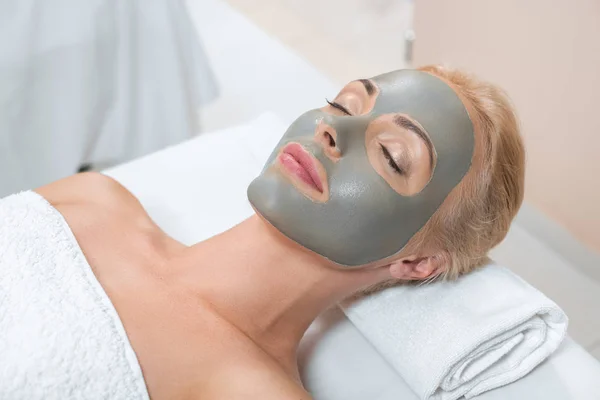 Close up of blonde woman lying with facial clay mask in spa — Stock Photo