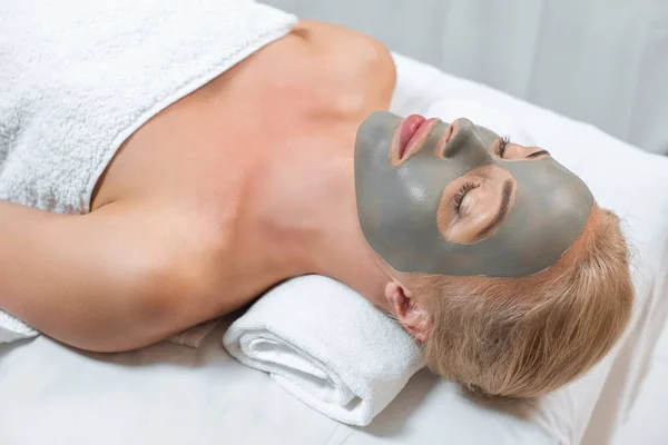 Close up of woman lying with closed eyes and facial clay mask in spa — Stock Photo