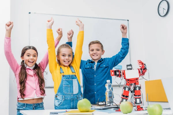 Compañeros de clase felices lanzando las manos en el aire y regocijándose después de la clase de robótica STEM - foto de stock