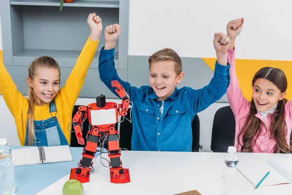 Cheerful classmates throwing hands in air after STEM robotics lesson — Stock Photo