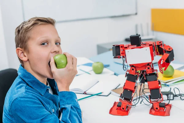 Menino alegre comendo maçã após lição de robótica STEM — Fotografia de Stock
