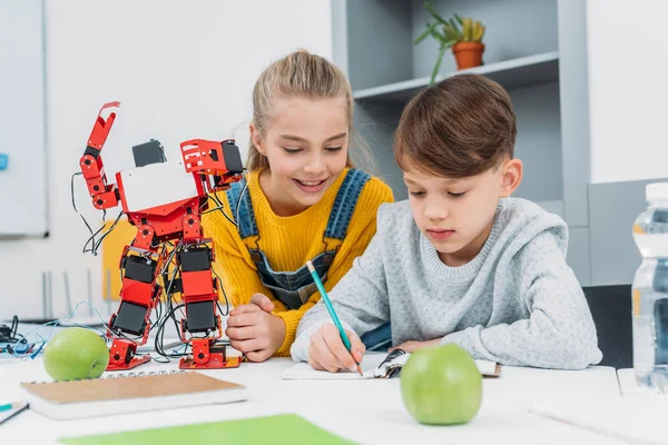 Schoolchildren writing in notebook at STEM robotics lesson — Stock Photo