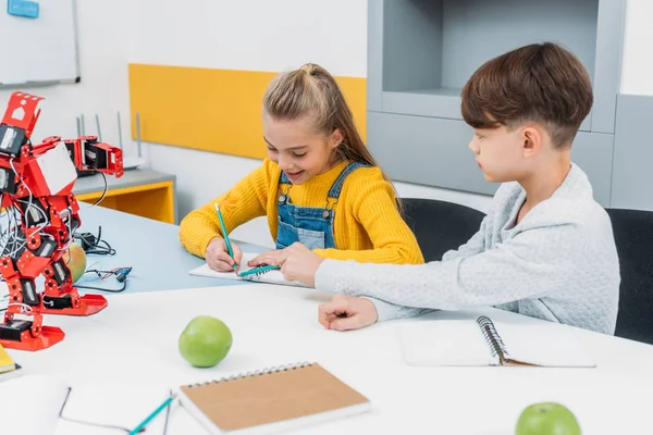Children writing in notepads at STEM robotics lesson — Stock Photo
