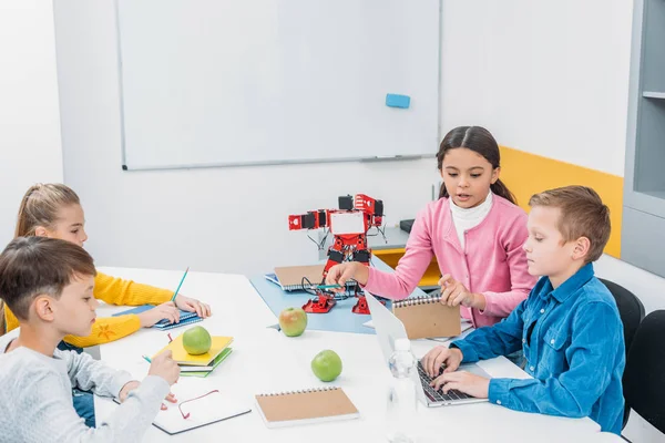 Children writing in notebooks and using laptop in stem class — Stock Photo
