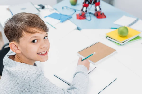 Colegial sonriente sentado en el escritorio y mirando a la cámara en el aula - foto de stock