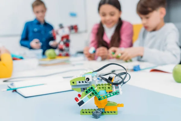 Multicolored handmade robot at desk with schoolchildren at background in stem class — Stock Photo