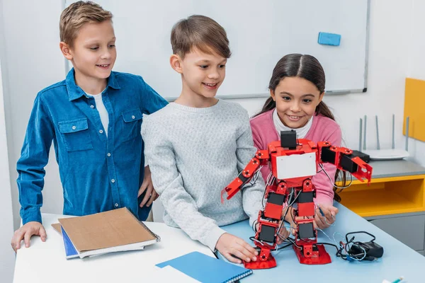 Escolares felizes tocando robô artesanal vermelho na mesa em aula de tronco — Fotografia de Stock