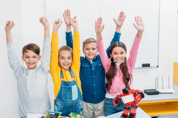 Happy schoolchildren raising hands and looking at camera in stem class — Stock Photo