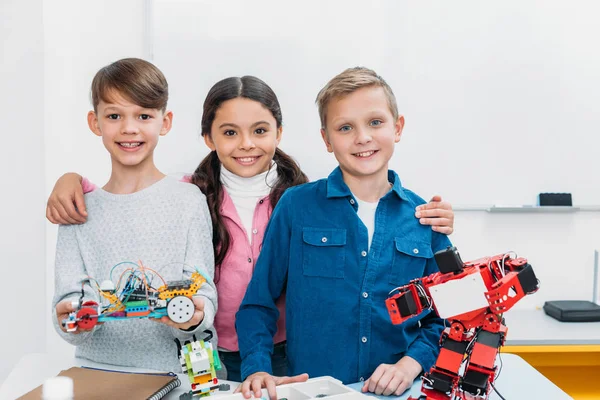 Heureux écoliers tenant robot électrique et regardant la caméra dans la classe de tige — Photo de stock