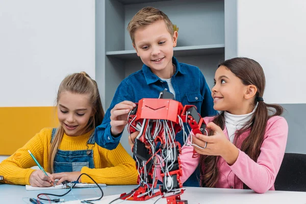 Des écoliers souriants fabriquant un robot électrique en classe de tige — Photo de stock