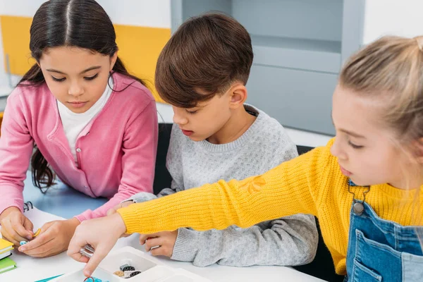 Écoliers assis au bureau et tenant des détails dans la classe d'éducation de la tige — Photo de stock