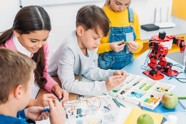 Schoolchildren making red robot with details and electric kit at desk in stem education class — Stock Photo