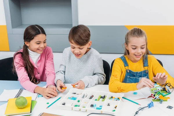 Crianças felizes sentadas na mesa e construindo robô na aula de educação de tronco — Fotografia de Stock