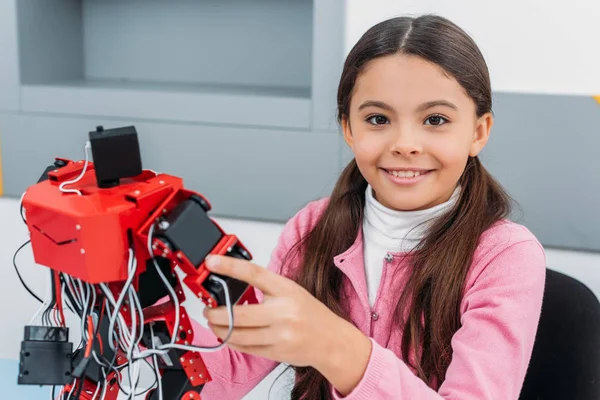 Close up view of schoolgirl smiling, holding red handmade robot and looking at camera in stem class — Stock Photo