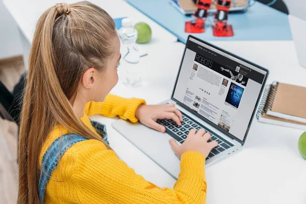 Школярка, використовуючи ноутбук з науки веб-сайт на екрані і читання статті про роботів — стокове фото
