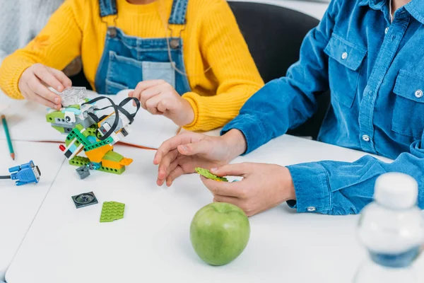 Cropped view of schoolchildren making robot with details at desk in stem class — Stock Photo