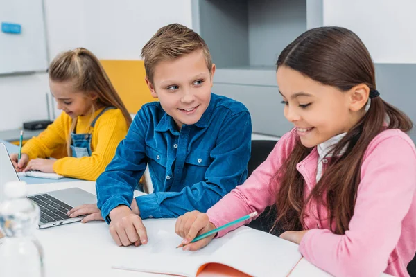 Colegial y colegialas escribiendo en cuadernos y utilizando el ordenador portátil durante la lección de tallo - foto de stock