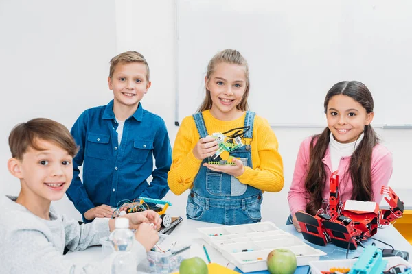 Niños felices de pie en el escritorio con robots en la clase de tallo - foto de stock