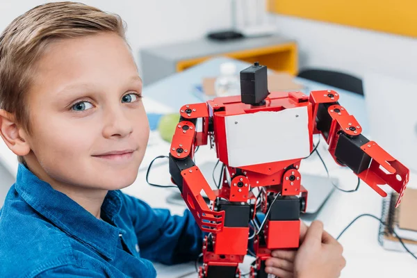 Lächelnder Schuljunge mit rotem Roboter und Blick in die Kamera in der Klasse — Stockfoto