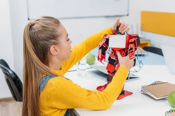 Colegiala tocando robot rojo hecho a mano en el escritorio en la clase de educación tallo - foto de stock