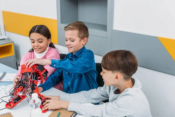 Lächelnde Schulkinder berühren roten Elektroroboter auf Schreibtisch im Unterricht — Stockfoto