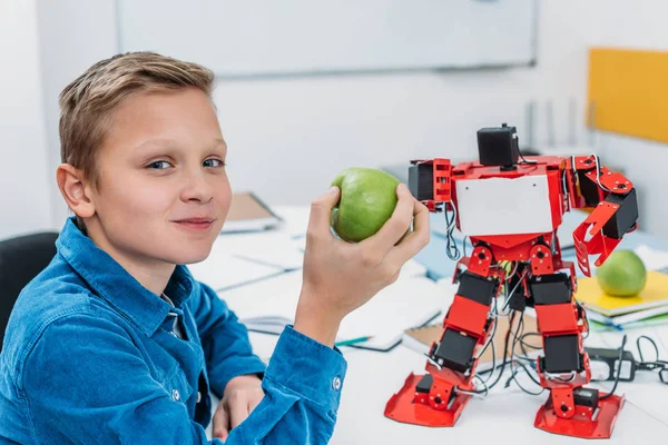 Smiling schoolboy holding green apple and looking at camera during stem lesson — Stock Photo