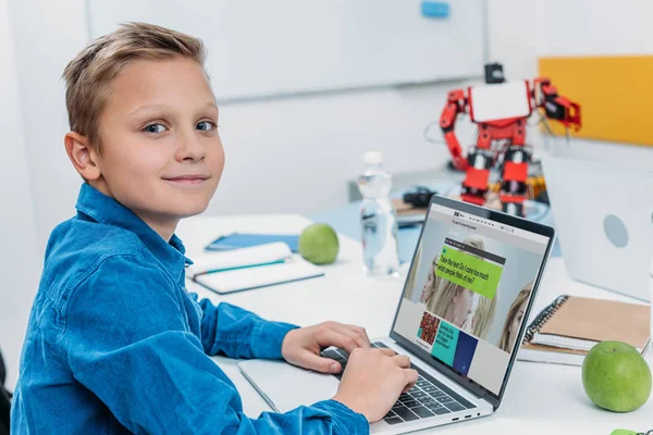 Niño sonriente usando el ordenador portátil con el sitio web de ciencia en la pantalla y tomando prueba psicológica - foto de stock