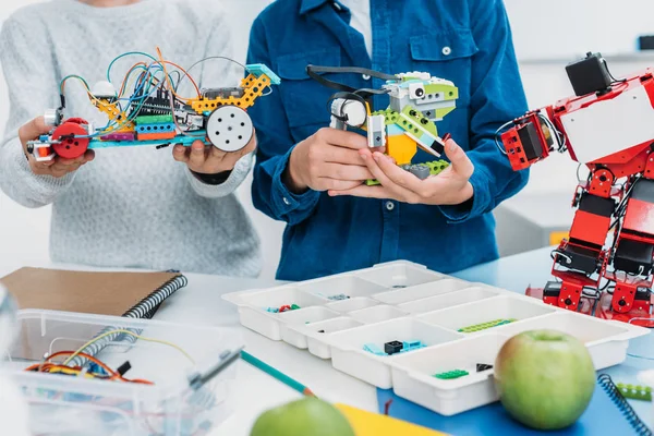 Vista recortada de los colegiales sosteniendo robots hechos a mano en clase de tallo - foto de stock