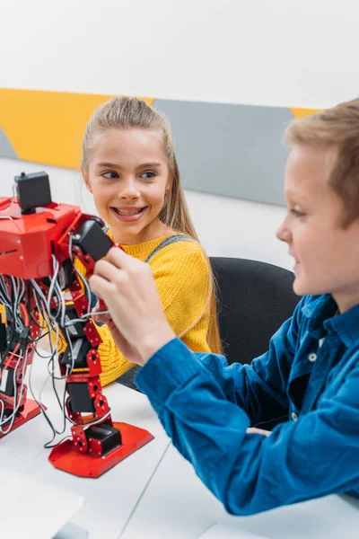 Sonrientes escolares programando robot juntos durante la clase de educación STEM - foto de stock
